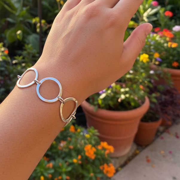 A silver-toned metal cuff bracelet with three interlocking circular links, shown worn on a person's wrist against a textured beige carpet background.